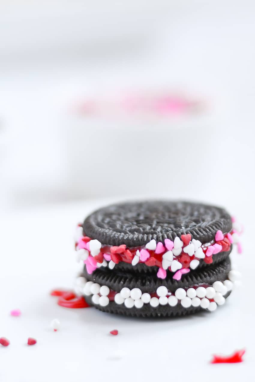 A stack of Oreo cookie decorated with red icing and valentine themed sprinkles for Valentine's Day