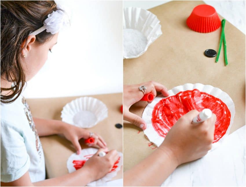 Child coloring coffee filters with red marker and materials to make paper poppy craft in background