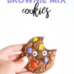 Chocolate brownie cookies with green, purple, and orange, M&Ms, plus candy eyes on a white background