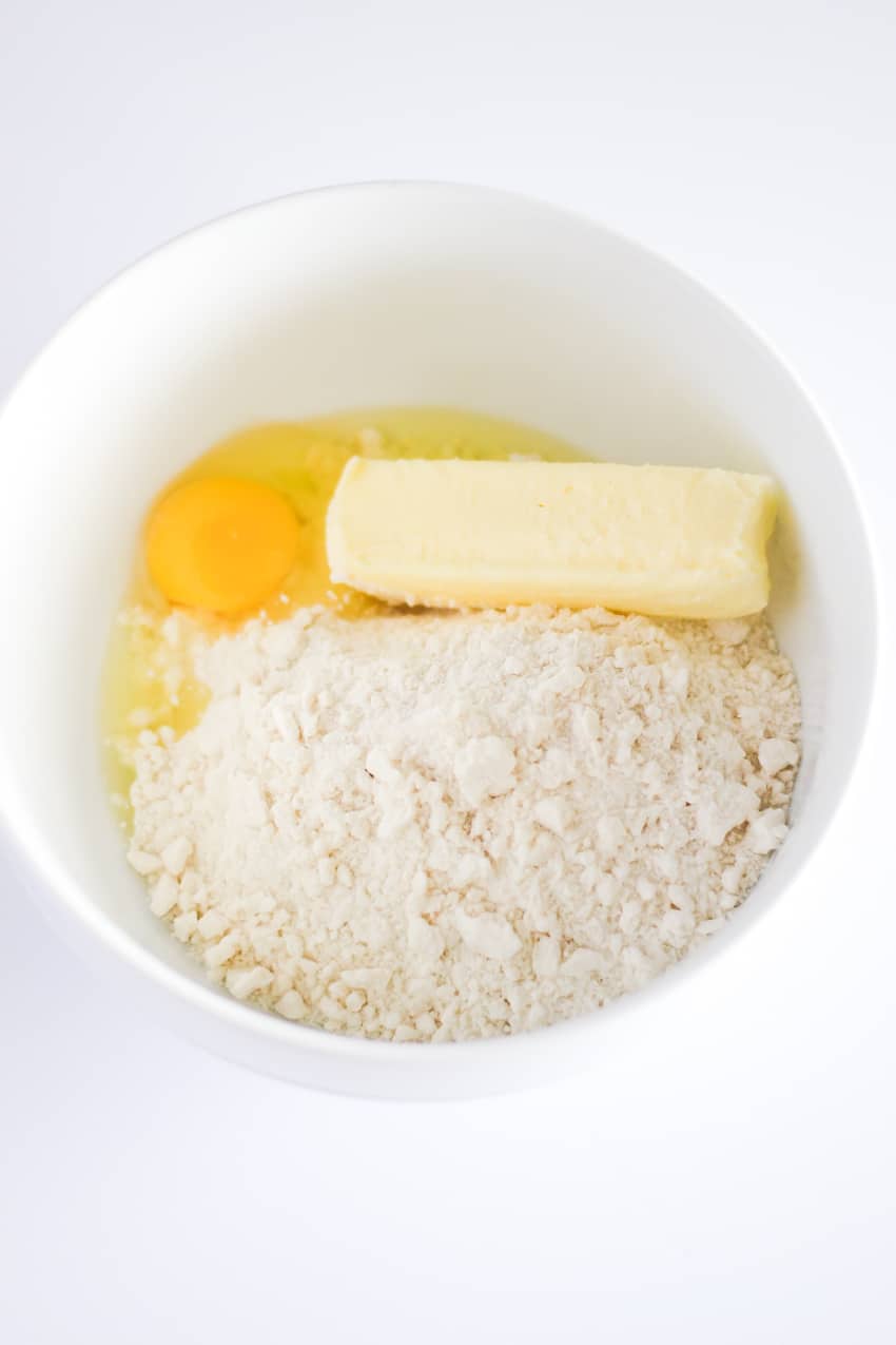 An egg, stick of butter, and sugar cookie mix in a round white bowl