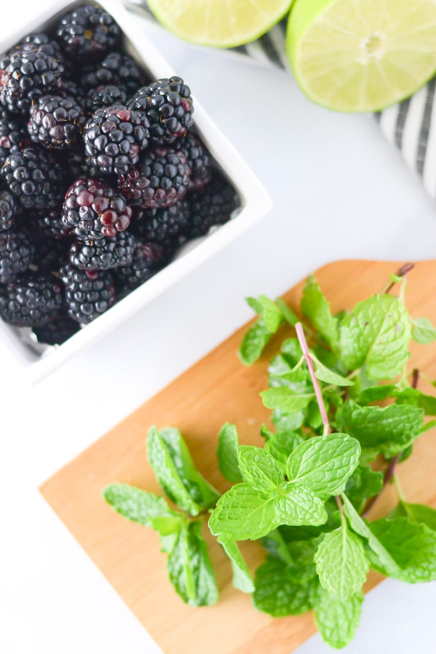 basket of black berries along side several springs of mint on a wood cutting board