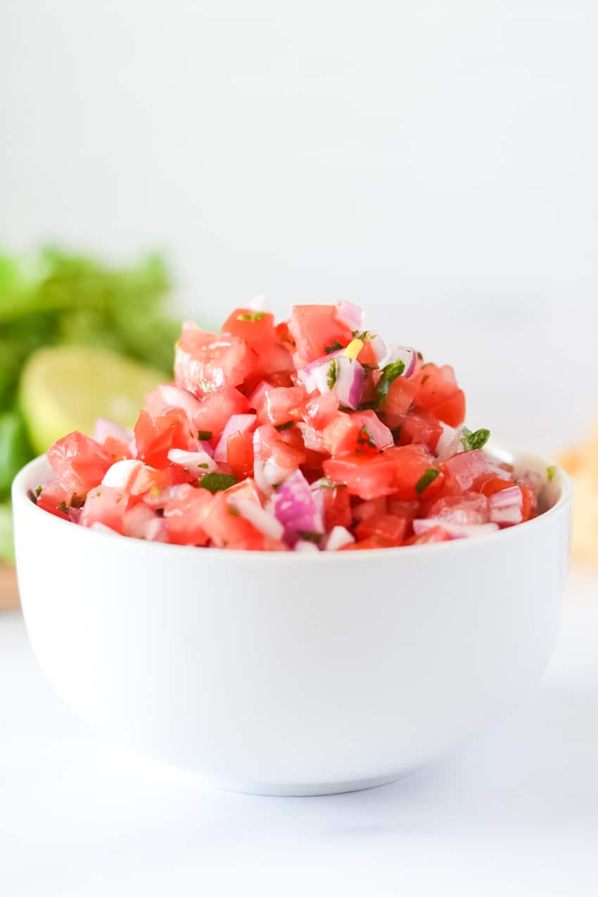 Close up of bowl of pico de gallo, made with roma tomatoes, red onion, and specs of cilantro