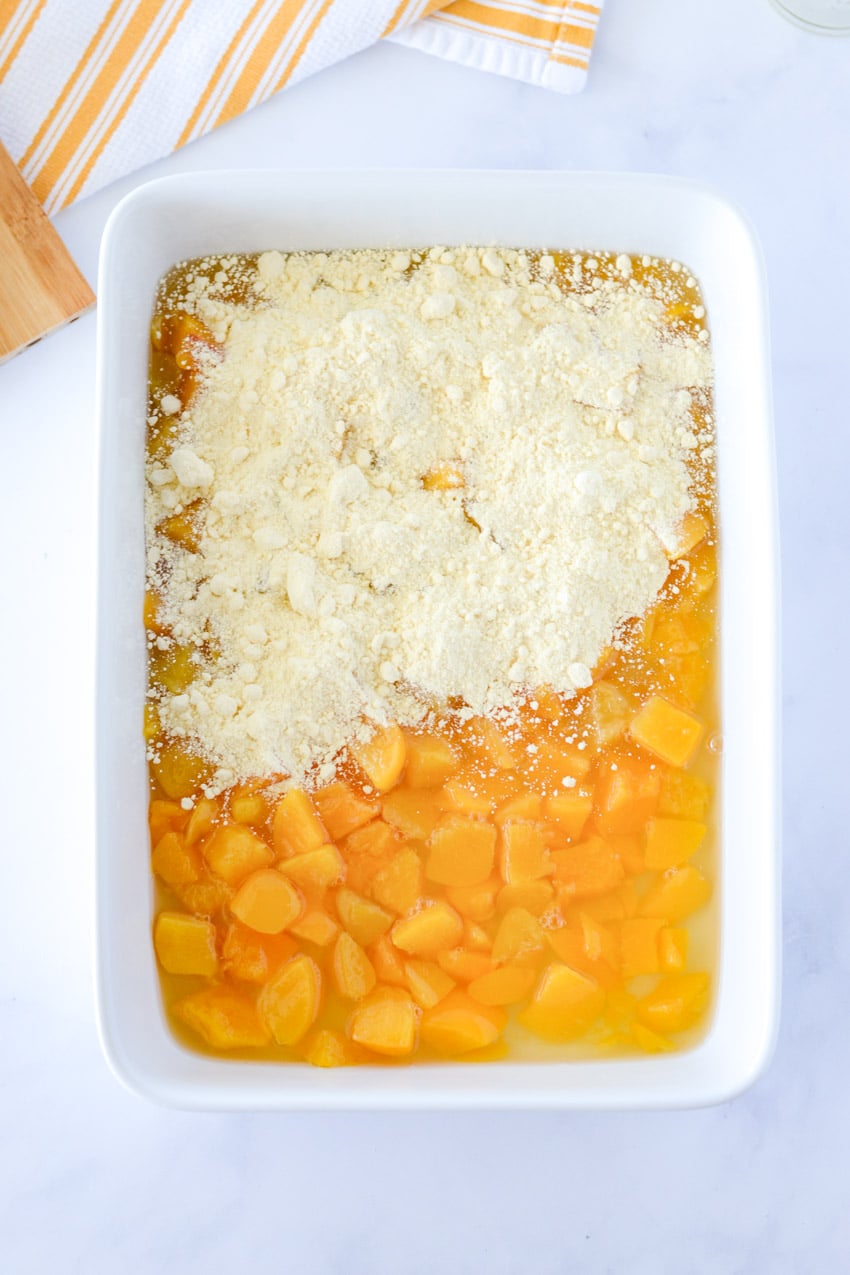 Boxed cake mix sprinkled over half of peach topping in a white 13x9 baking dish