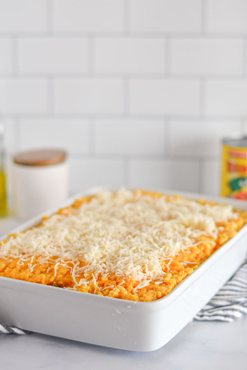White baking dish filled with yellow imperial rice mixture and topped with shredded mozzarella cheese