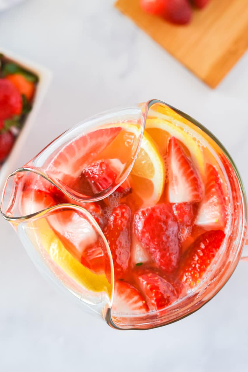 Top view of sliced strawberries and lemons floating in a glass pitcher 