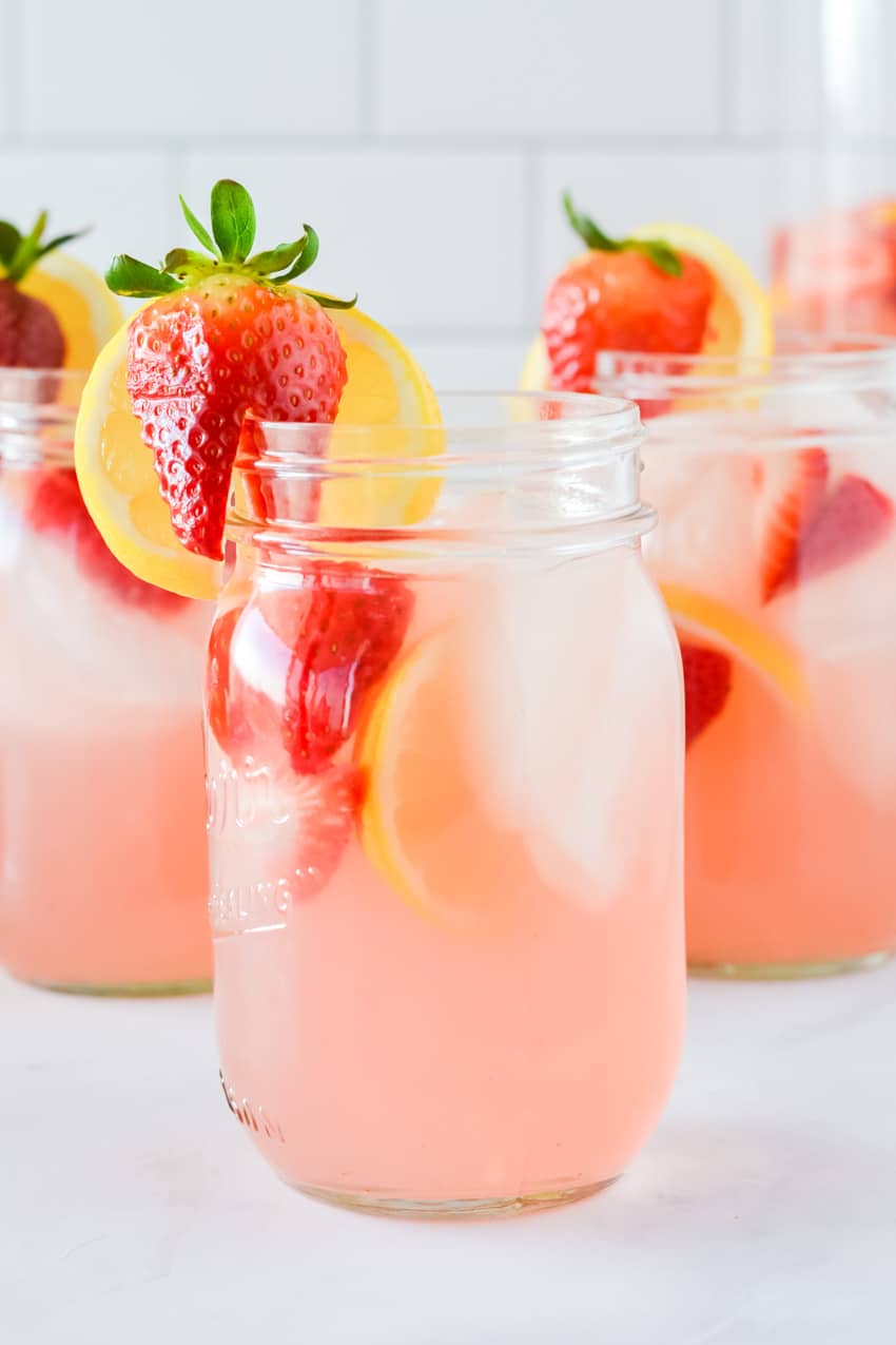 Close up of a mason jar with pink lemonade moscato punch with lemons and strawberries as garnish on the rim
