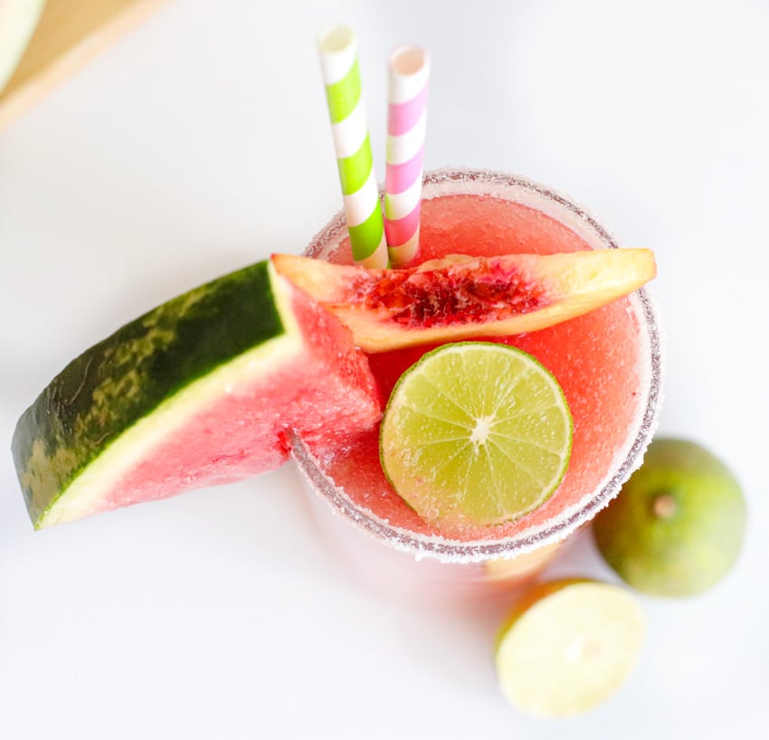 Top view of a Watermelon Peach Daiquiri in a glass, garnished with a slice of watermelon, peach, and lime