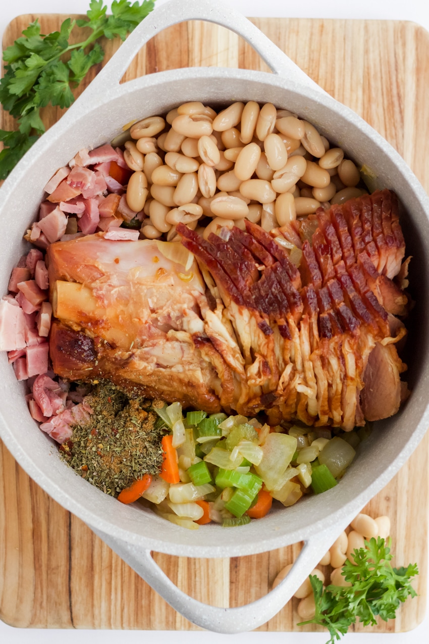 Ham bone and ingredients (carrots, celery, onion, beans) in a large white stock pot for ham and bean soup. 