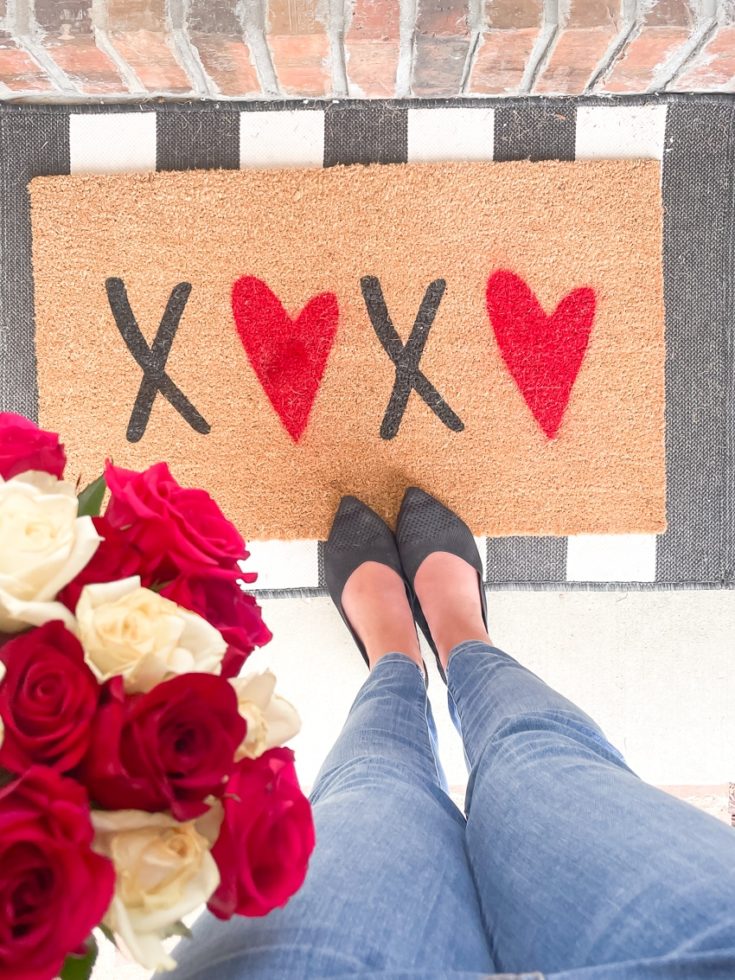 Top view of XOXO doormat layered on a black and white mat with a bunch of red, pink, and white, roses