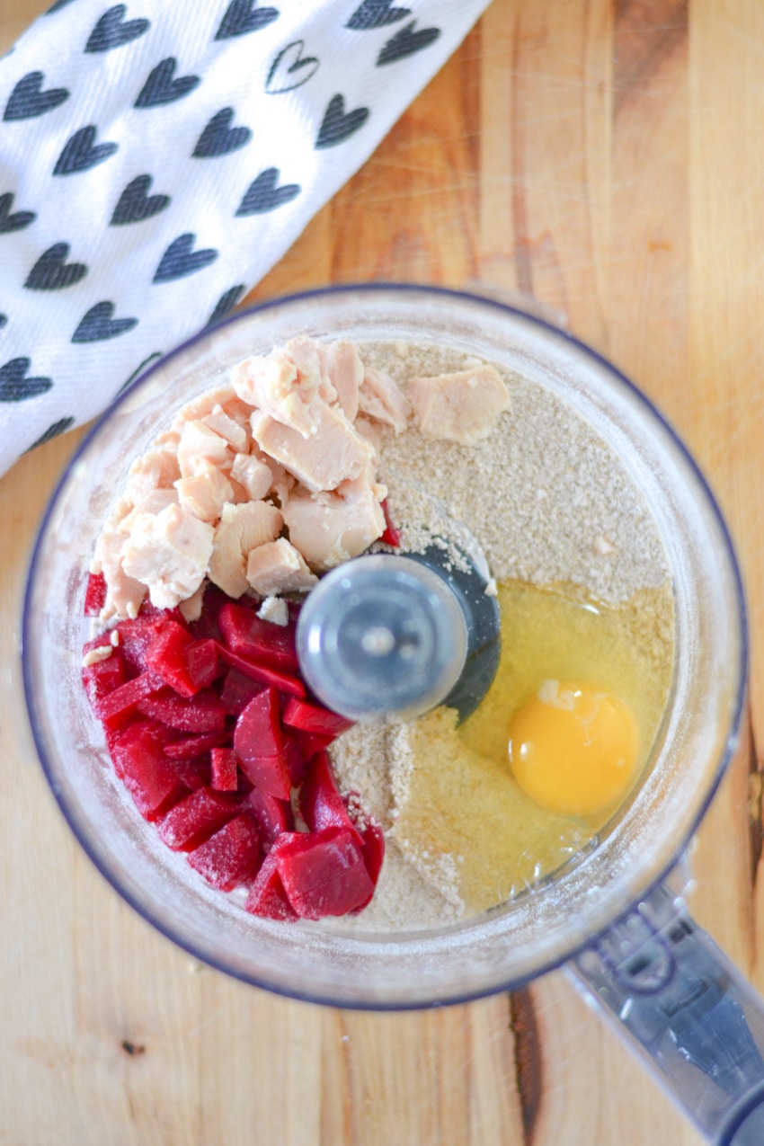 diced chicken, diced beets, and a cracked egg sitting a top ground oatmeal in a food processor