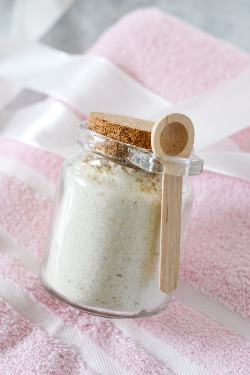 Glass jar of diy powdered milk bath mixture with wooden spoon on a light pink towel