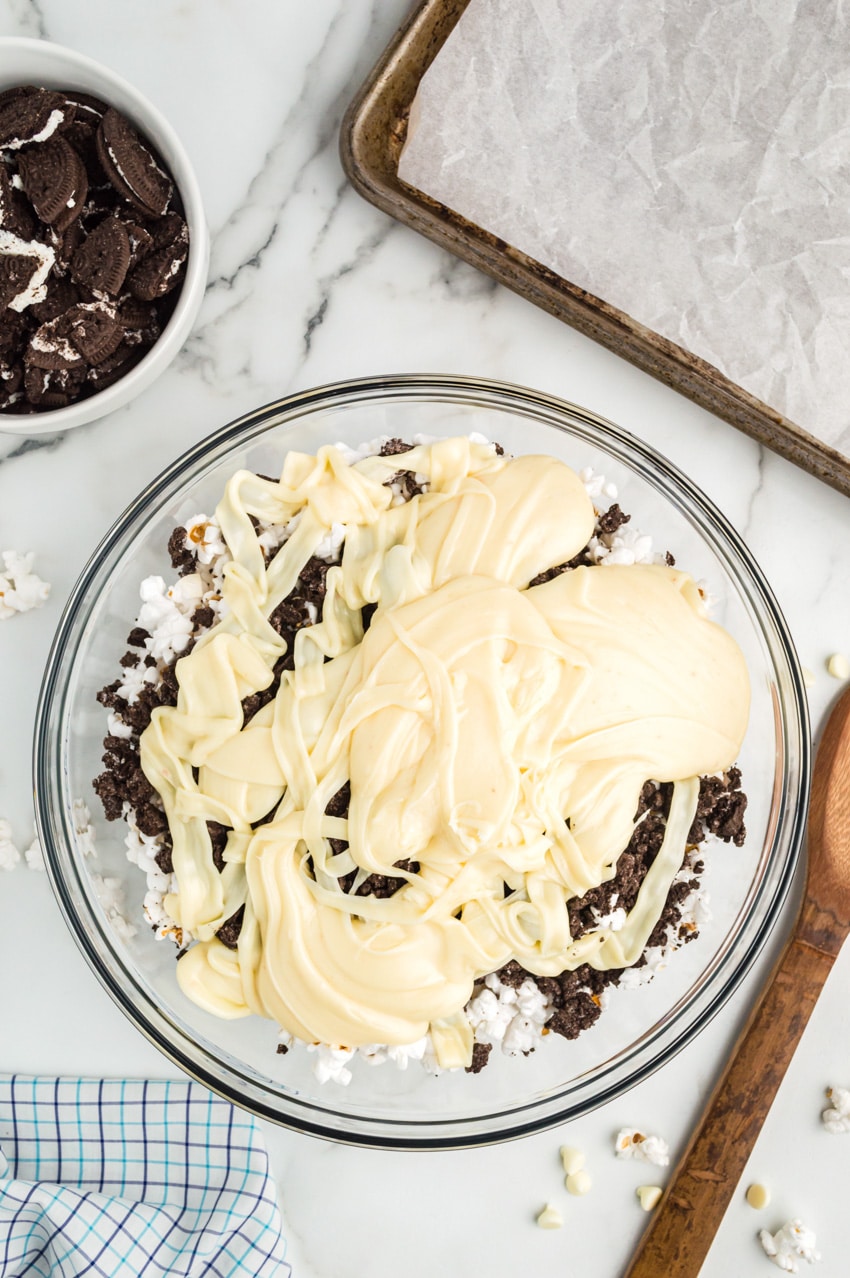 bowl of crushed oreos off to side of large bowl filled with popcorn, oreo chunks, and melted white chocolate