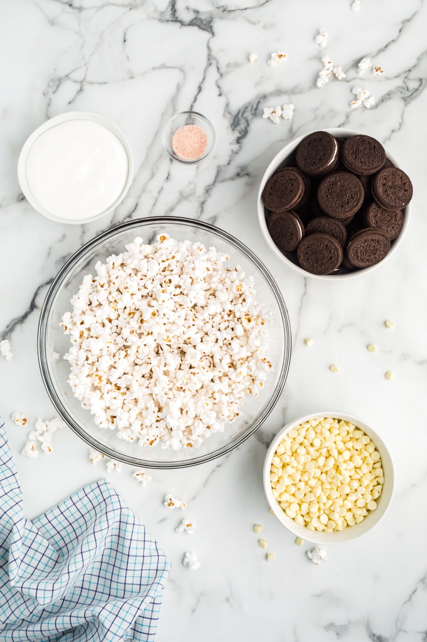 Ingredients for oreo popcorn separated into bowls on marble countertop