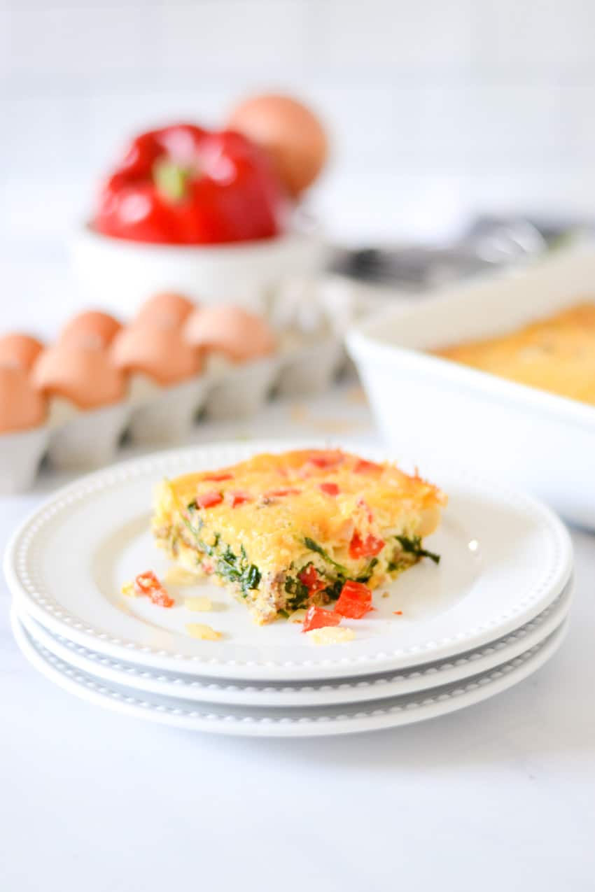 Slice of breakfast casserole on a white plate with ingredients behind