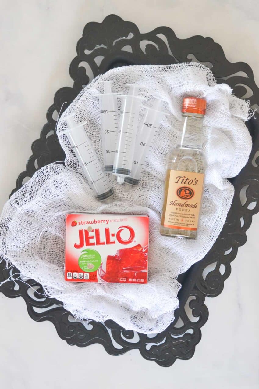 Empty plastic syringes and strawberry Jello box and Tito's vodka on a spooky tray