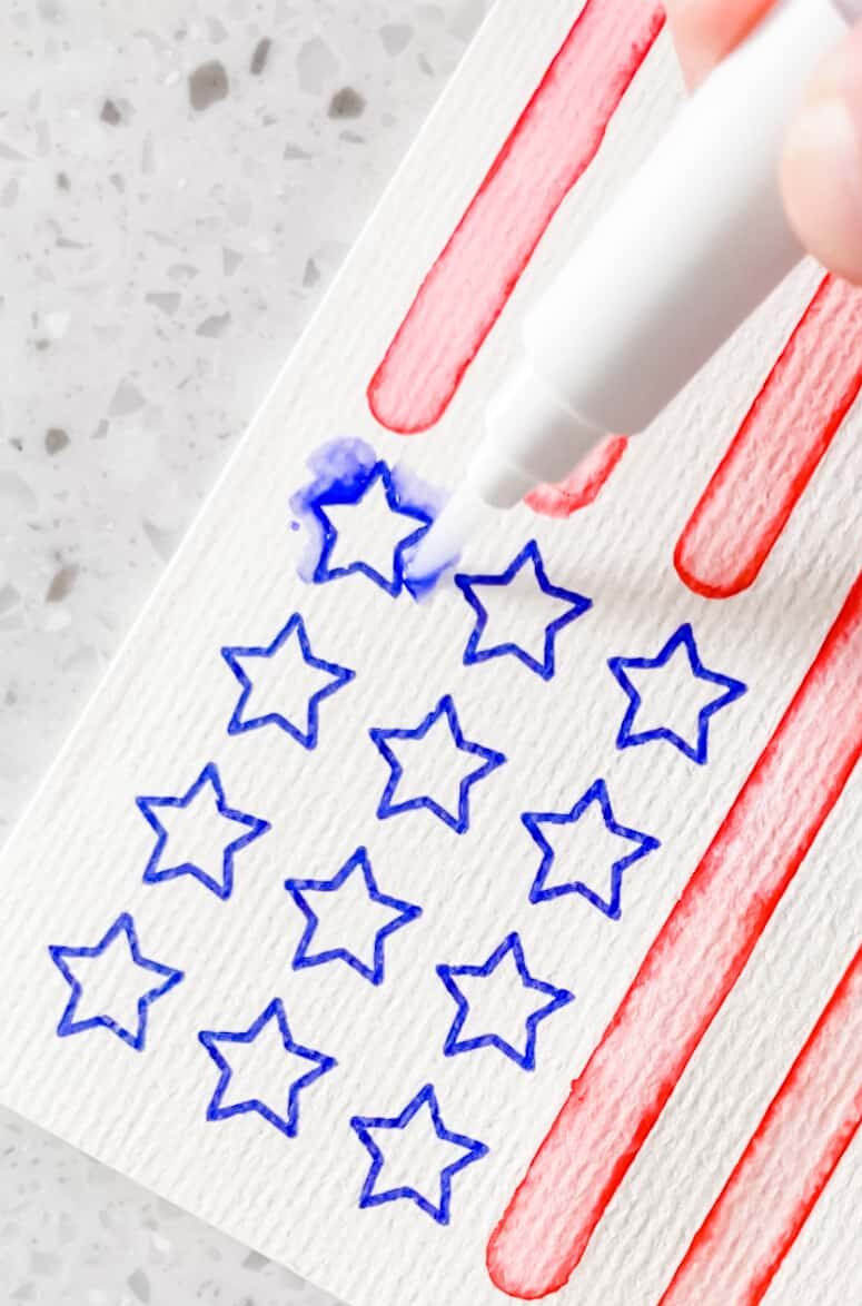 Tip of watercolor brush blending blue star on American flag card