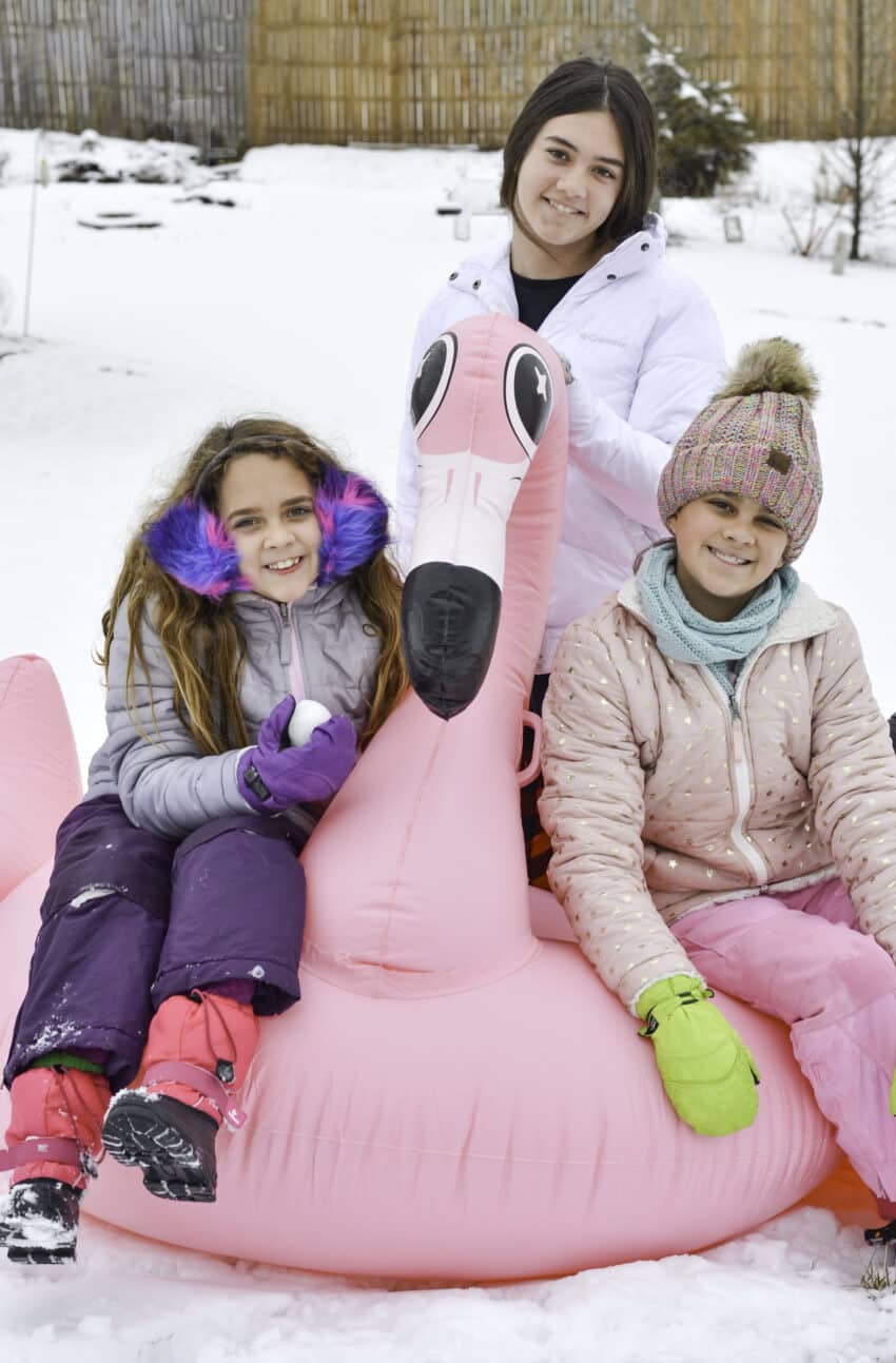 Three girls sitting on a large flamingo inflatable in the snow