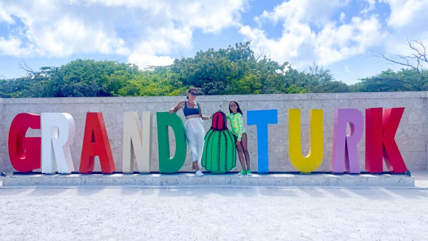 Two people posing at the Grand Turk sign, that spells out "Grand Turk" in colorful letters
