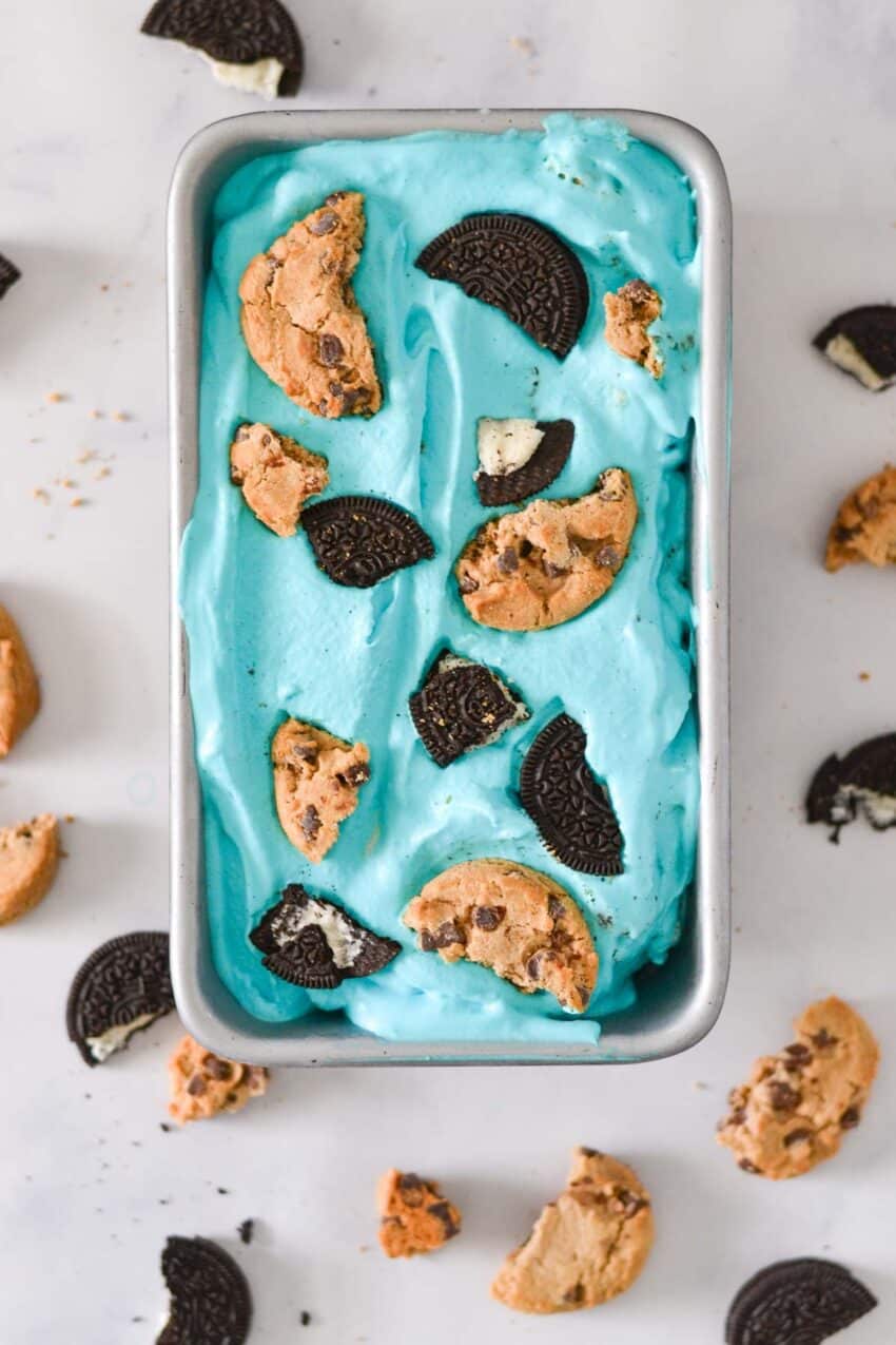 Loaf pan of blue ice cream with pieces of Oreo and chocolate chip cookies mixed in