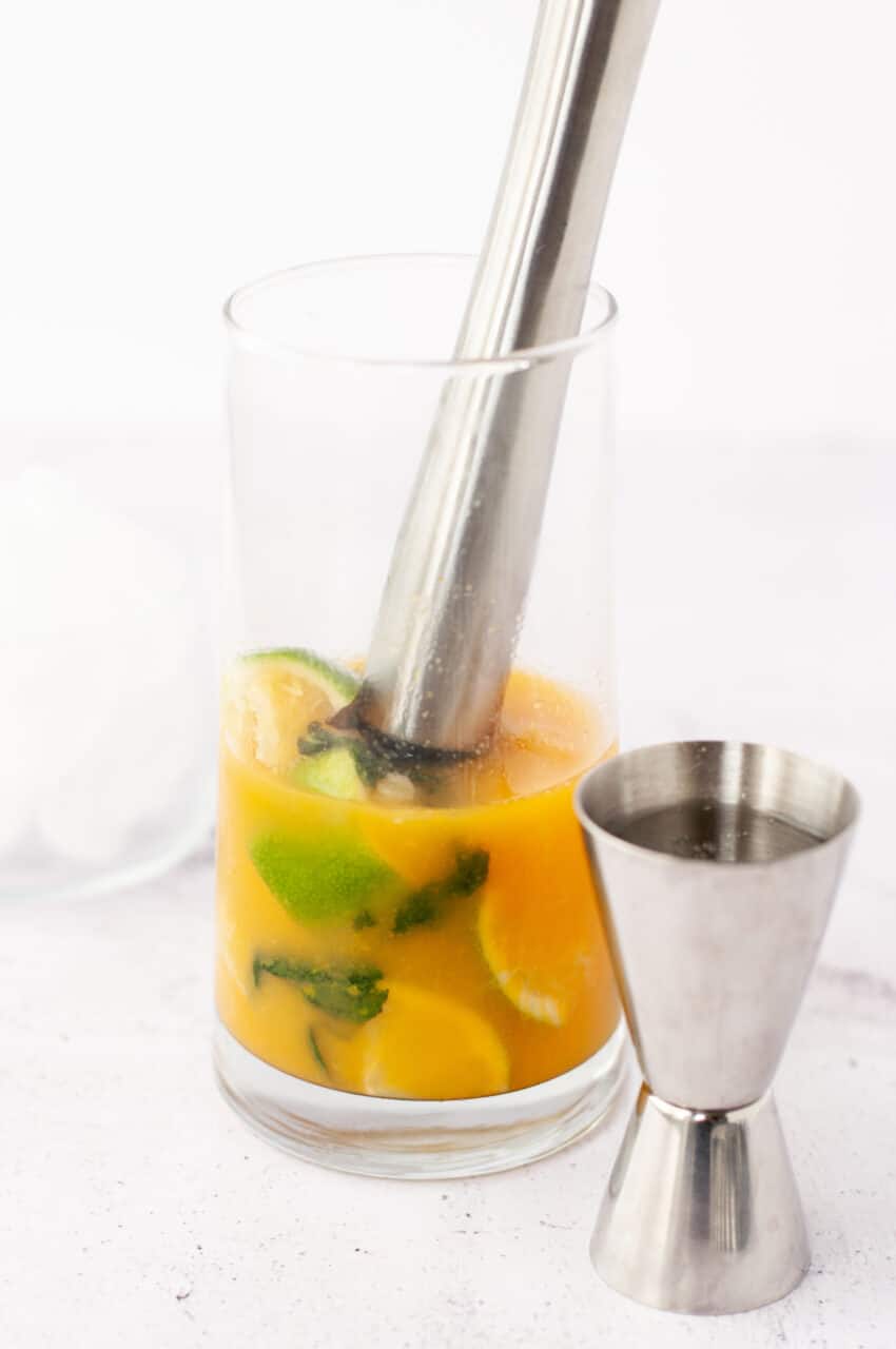 Muddling passion fruit, lime wedges, and mint in a cocktail glass