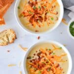 Two white bowls filled with potato soup and garnished with bacon, shredded cheddar cheese, and green onions