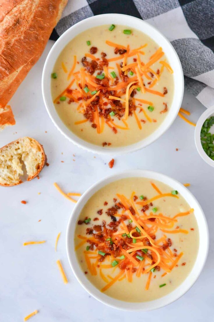 Two white bowls filled with potato soup and garnished with bacon, shredded cheddar cheese, and green onions