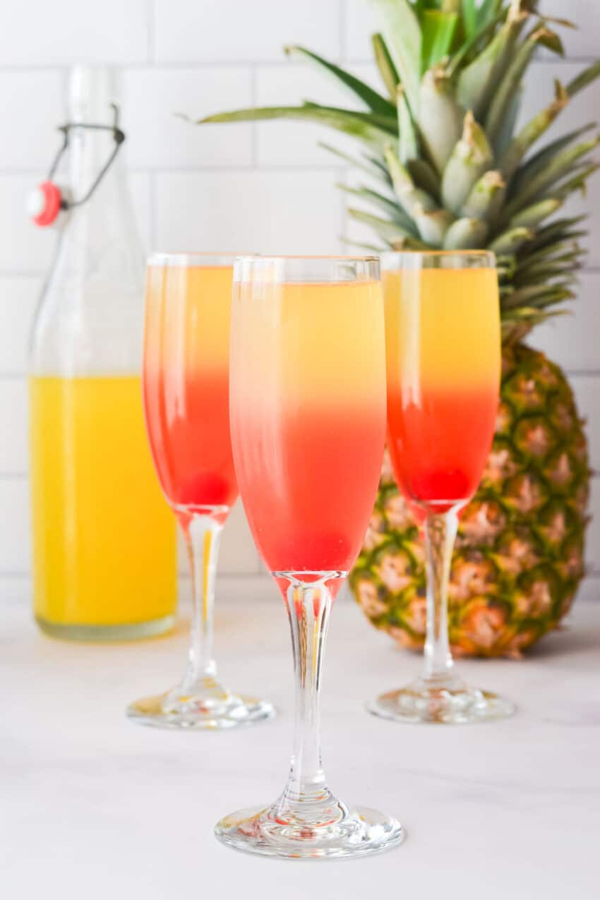 Three champagne flutes filled with layered pineapple mimosa