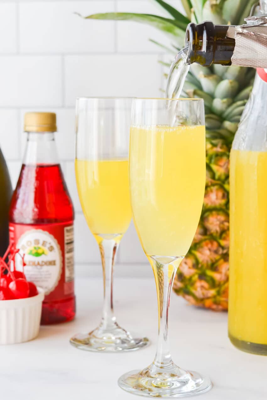 Pouring Prosecco into champagne flutes filled with pineapple juice