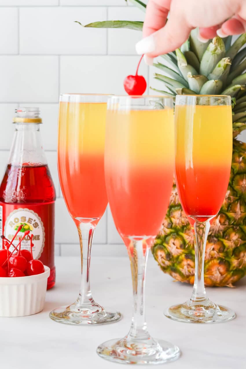 Dropping a maraschino cherry into a layered Pineapple and Grenadine mimosa.