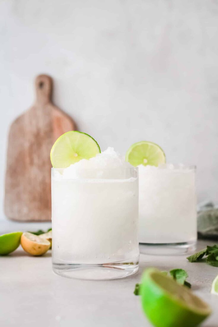 Two rocks glasses filled with Frozen Caipirinha and topped with lime rounds.
