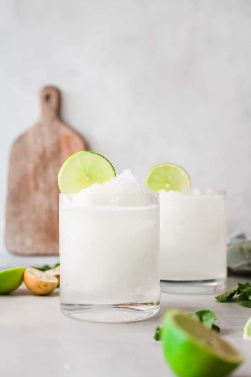 Two rocks glasses filled with Frozen Caipirinha and topped with lime rounds.
